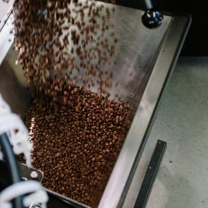 Close-up of coffee beans being poured into a roasting machine, showcasing industrial coffee production.