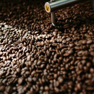 Detailed view of coffee beans in a roasting machine with steel arm inside a professional roaster.