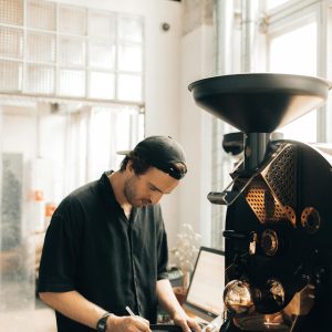 Man operating coffee roaster in a modern cafe, focusing on coffee production.