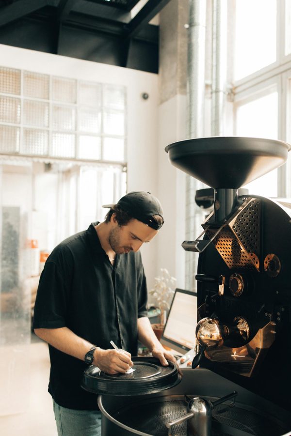 Man operating coffee roaster in a modern cafe, focusing on coffee production.